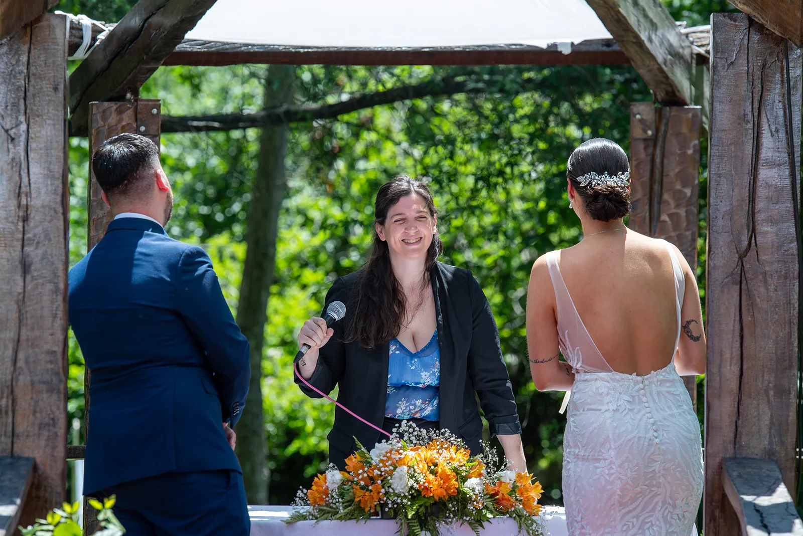 La oficiante sonríe entre los novios durante la ceremonia